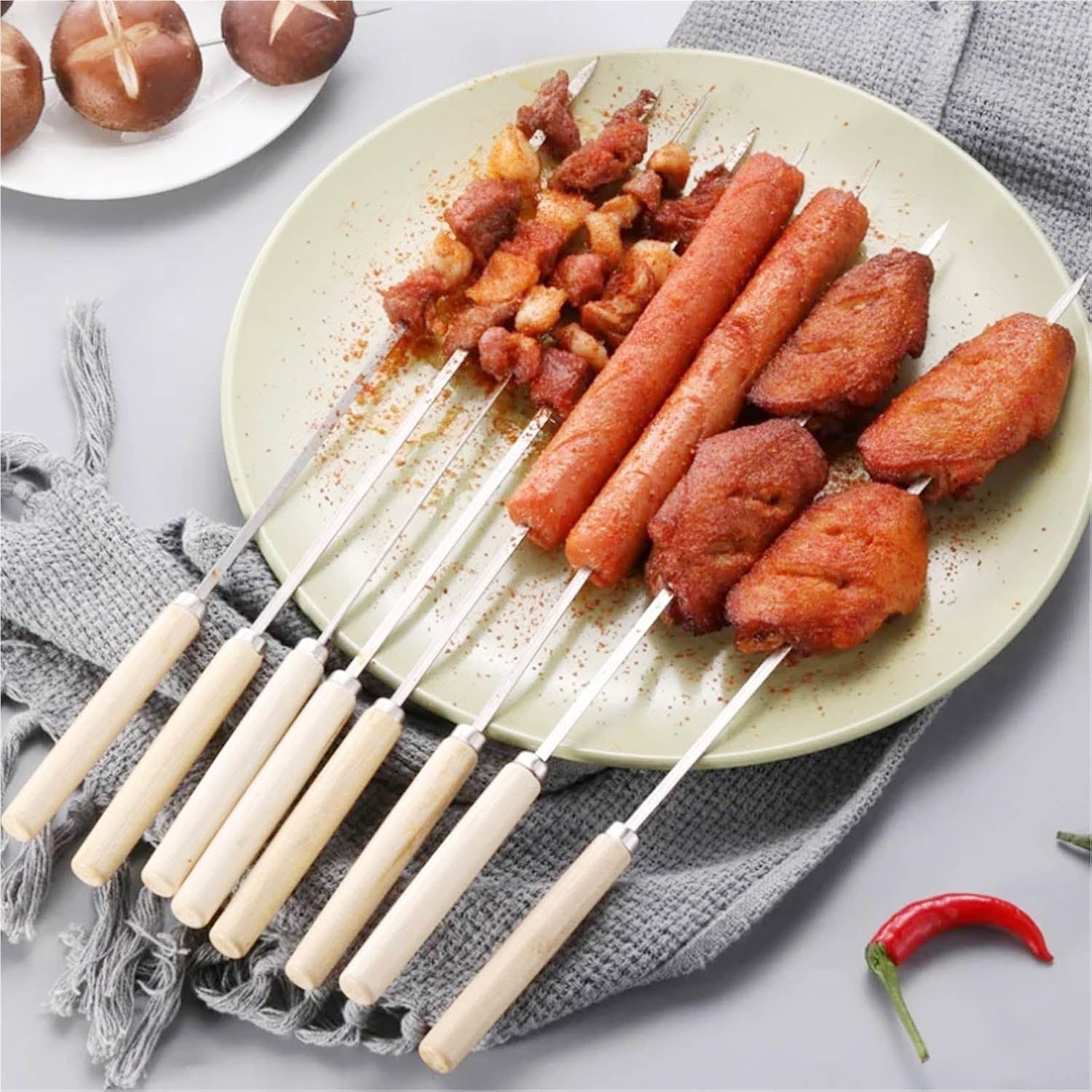 Cooked meat, sausages, and chicken wings threaded onto metal skewers with wooden handles, served on a green plate.