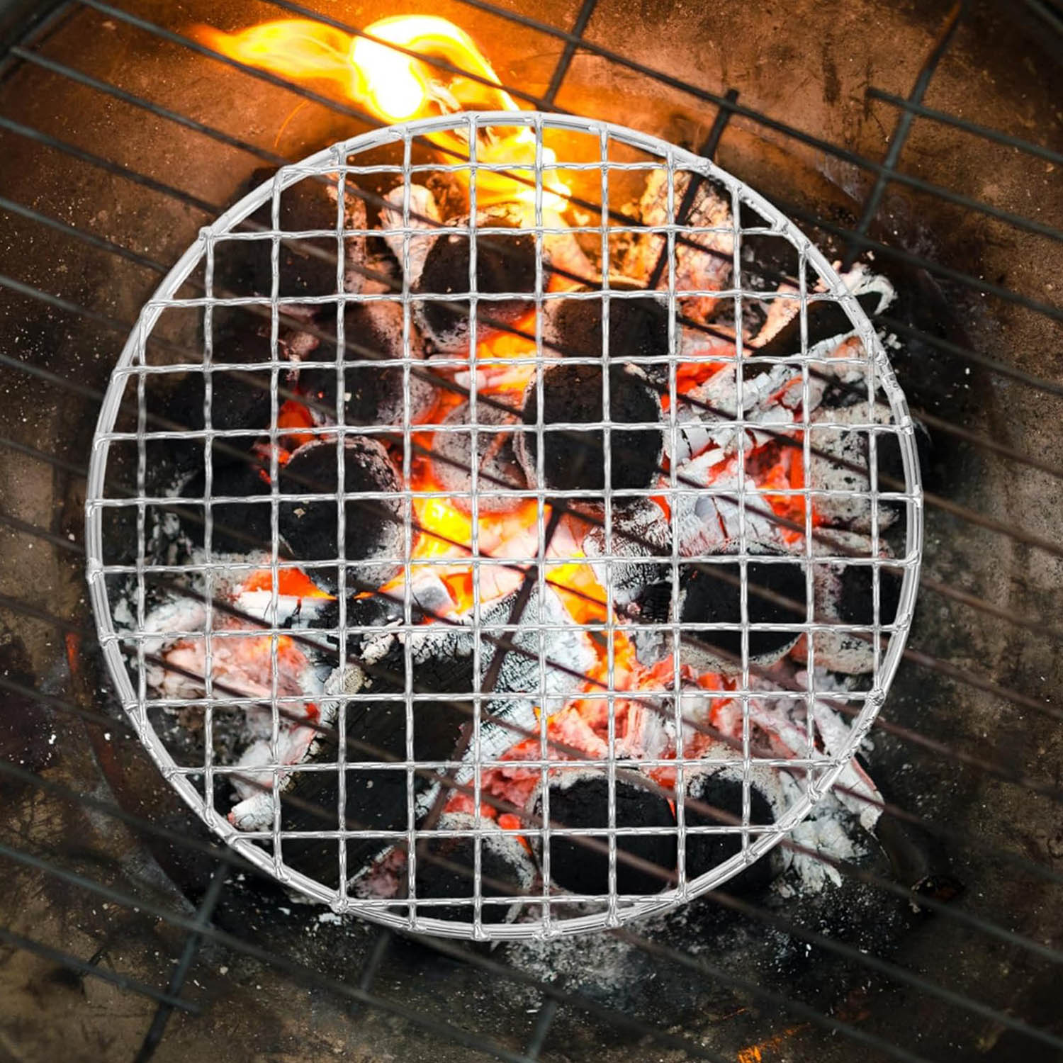 Top-down view of a small round wire mesh grate placed over glowing orange charcoal embers in a fire pit.