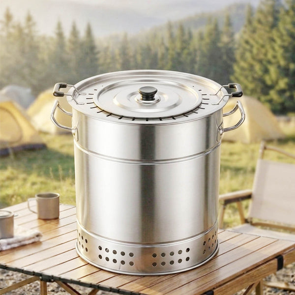 A stainless steel vertical charcoal grill on a wooden picnic table, features side handles and a vented lid, in a forest camping setting.