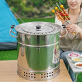 A woman in a tent camping ground holds colorful skewers next to a stainless steel vertical charcoal grill on a wooden table.