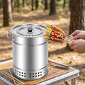A hand holding various colorful skewers near a stainless steel vertical charcoal grill on a wooden table in a forest.